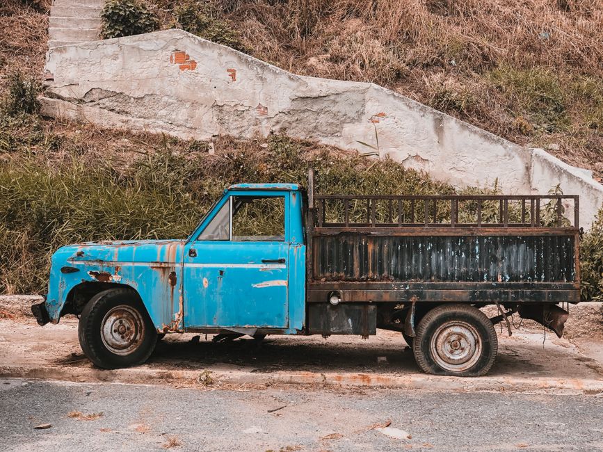 A vintage blue pickup truck parked beside a rustic stone wall, exuding a sense of nostalgia and decay.